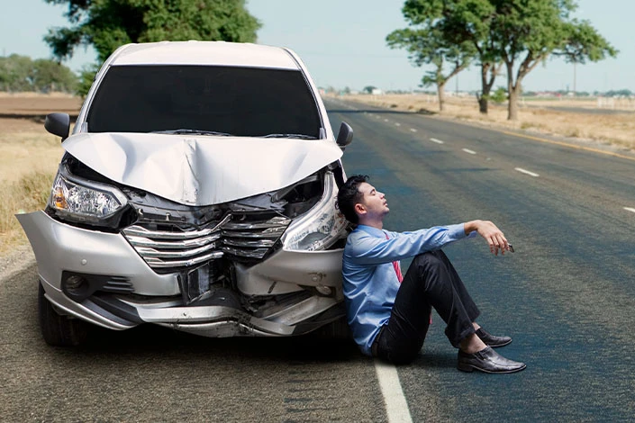 Frustrated man sitting next to his totaled vehicle after a Wyoming car accident.