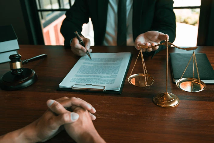 A big rig accident lawyer in a dark suit fills out paperwork at a desk adorned with the scales of justice while helping a Wyoming truck crash victim.