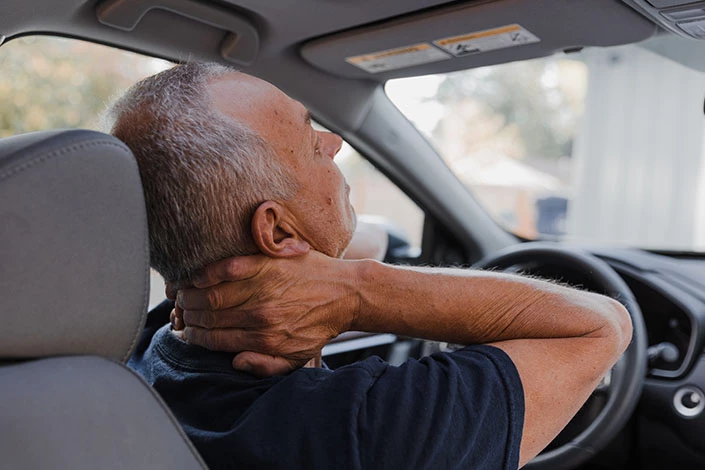 A man with a neck injury after car accident rubbing the sore area while sitting in his vehicle.